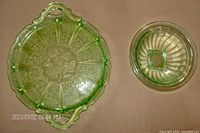 Top down view of the green Cherry Blossom pattern depression glass tray and the green Vaseline uranium glass mixing bowl laid out side by side.