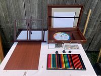 Overview of entire art set showing wooden box with supplies, paper holder, sketch pad and pencils spread out on table.