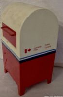 Three-quarter view of red and white Canada Post mailbox coin bank showing logo and coin slot