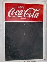 Full front view of the vintage metal Coca Cola chalkboard sign showing the logo and chalkboard area with white border and minor rust on bottom edge.