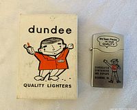 Lighter alongside original white Dundee Quality Lighters box featuring cartoon figure in red jacket holding lighter.