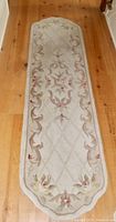 Top-down view of the beige wool hall carpet runner laid on a wooden floor, showing the full length and floral pattern with circular bordered ends.