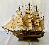 Front view of handcrafted wooden sailing boat model with three masts, striped sails, rigging, and base stand with name plaque.