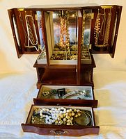 Multiple views of a large wooden multi-layer jewelry box with etched glass front and mirrored interior, showing the arranged vintage jewelry inside including necklaces hanging on hooks, two drawers open displaying rings, bracelets, brooches and other items.