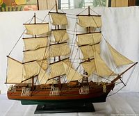 Front view of the handcrafted wooden sailboat model showing three masts with fabric sails and detailed rigging, mounted on a stand.