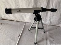 Front angle view of the white Orbitor telescope mounted on an aluminum tripod, black details and four rubber feet on tripod legs visible.