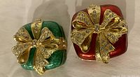 Photo of green and red enamel trinket boxes topped with gold-tone crystal encrusted bows.