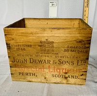Wooden box showing text on one side with 'John Dewar & Sons Ltd.', 'Established 1846', 'Awarded 50 Medals', and 'Special Liquor'.