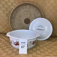 Corelle stoneware casserole dish with fruit pattern and lid, placed in front of the woven serving tray