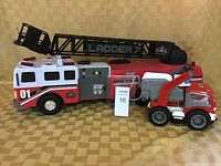 Side view of large red and white fire ladder truck showing 'LADDER 7' marking and smaller fire truck next to it.