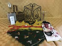 Photo showing all the kitchen items including an apron with rooster print, woven basket with utensils, metal cookbook holder, measuring cup, and kitchen towel.