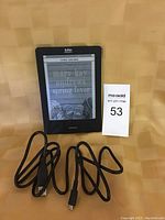 Photo of Kobo e-reader with screen on showing a book cover, alongside two charging cables.