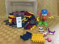 Clear plastic container holding assorted colorful linking track pieces and a Mr. Potato Head toy with facial and hand parts laid out nearby.