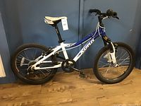 Side view of child's blue and white Kona mountain bike showing frame, tires, saddle, and handlebars.