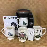 Photo showing Bosch Tassimo coffee maker with four Susan William-Ellis ceramic mugs featuring butterfly and floral designs arranged in front.