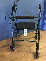 Front view of the dark green folding walker with padded seat and handles, showing the four wheels and frame.