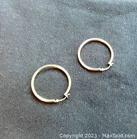 Pair of small 10K gold hoop earrings laid flat on a black fabric background showing the entire hoops.