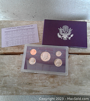 Photo of the coin set showing the penny, nickel, dime, quarter and Kennedy half dollar displayed in a hard plastic case with purple backing, plus the certificate card and purple cover with US seal.