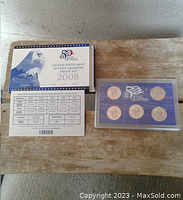 Full view of the closed packaging, showing certificate, cover card, and hard plastic case with coins visible.