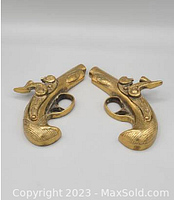 Pair of brass musket replicas facing each other showing engraved sides and trigger guards.
