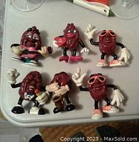 Photo showing six 1980s California Raisins plastic figures in various poses on a white surface, capturing details of each figure.