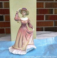 View of front side of Coalport figurine 'Jessica' in pink vintage dress with hat, standing next to original box.