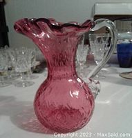Front angled view of cranberry glass pitcher showing textured and ruffled designs with clear handle.