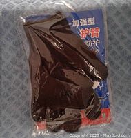 Photo showing black cut resistant gloves in sealed clear plastic package with blue and red backing card, on light blue textured surface.