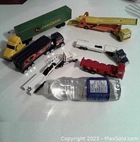 Photo showing 6 die cast trucks including John Deere trailer, yellow crane, black flame semi, red and white trucks, and NASA truck.