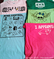 Five girls t-shirts with visible graphics in various colors: pink with tiger eyes, light blue with 'MIND CONTROL' faces, green with 'Diamond Spirit' text, light yellow-green with skull and wings, bright pink with 'I APPROVE' armadillo