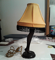 Replica leg lamp with attached electrical cord; lamp shade shows black fringe trim hanging at bottom.