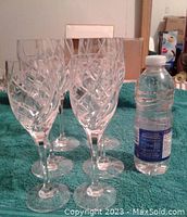 Six tall etched crystal champagne glasses shown standing upright next to a water bottle for size reference on a green cloth background.