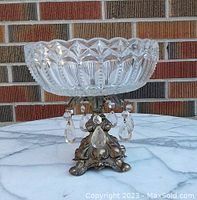 Front and side view of clear glass fruit bowl with hobnail edge and dangling glass jewels, metal ornate base visible.
