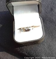Photo of titanium ring inside black jewelry box with white cushioning, showing ring's shiny polished surface and size.