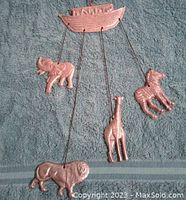 Full view of the Noah's Ark shaped top piece with four animal figures hanging from it: elephant, zebra, giraffe, lion. Arranged on a cloth background.