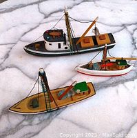 Photo shows three wooden boat models on a marble surface with visible loose black rigging strings on the boats.