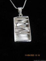 Close-up front view of rectangular chunky sterling silver pendant on black background, showing abstract textured waves