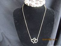 Silver necklace displayed on black stand. Features a double heart pendant with smooth silver outline.
