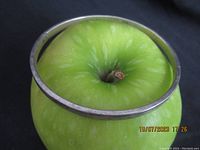 Photo of silver bangle placed around green apple showing its size and shape, vintage solid silver with some surface wear.