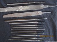 Overview of 13 metal files of varied lengths and shapes laid out on black background, showing signs of use and surface wear.