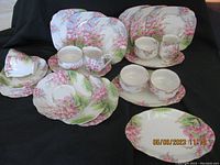 Full lot showing entire 22 piece set arranged on black backdrop with plates, cups, saucers, and creamers.