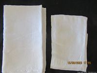 Two folded vintage linen damask tablecloths placed side by side on a black surface, one larger and one smaller.