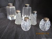 Photo showing three sets of vintage salt and pepper shakers with clear glass bodies and sterling silver tops, arranged on black background.