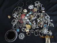 Top-down photo of assorted vintage costume jewelry including bracelets, rings, brooches, and earrings on black cloth.