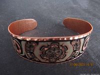 Full view of the copper bracelet showing the painted and etched Native art design across the band under lighting on a black cloth.