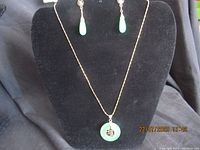Front view of the necklace with circular green jade pendant and matching earrings displayed on a black stand.