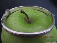 Small silver bangle bracelet shown over a green apple for scale. The bangle is circular and slim with a polished exterior showing some wear.
