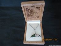 Wooden box with the silver chain necklace with whale tail pendant and jade inset displayed. Inside lid has printed information about jade.