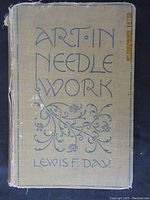 Front cover of the vintage book "Art in Needle Work" showing the title and author's name with decorative floral blue illustration on beige cloth cover.