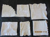 Seven vintage linens including round lace centerpieces, square centerpiece, hand towel, two tablecloths on black background.